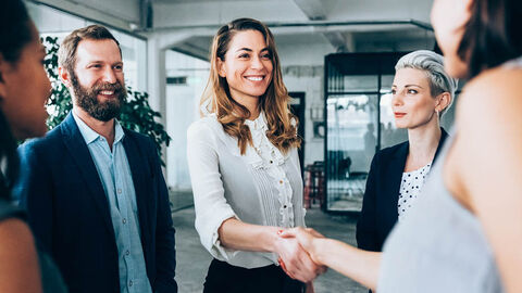 Eine Gruppe von Menschen, in der sich zwei Frauen die Hand reichen.