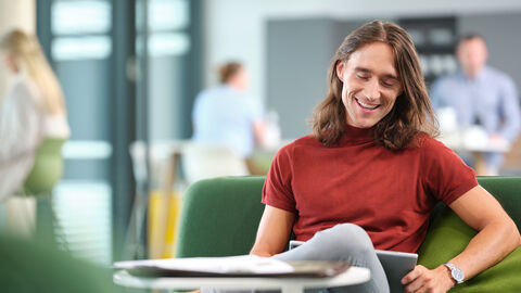 Auf dem Foto sitzt ein Jura Student lächelnd vor seinem Tablet.